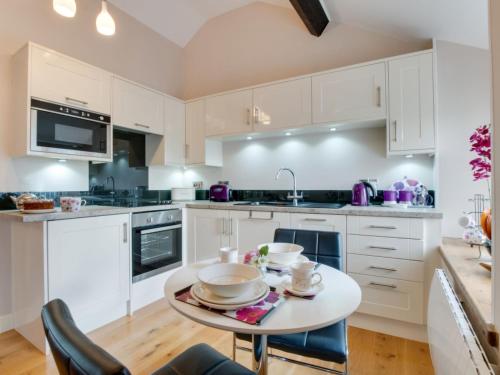 TrawsfynyddにあるHoliday Home Gandil by Interhomeの白いキャビネット、テーブルと椅子付きのキッチンが備わります。