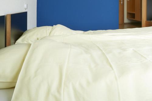 an unmade bed with white sheets and a blue wall at Youth Hostel Beaufort in Beaufort