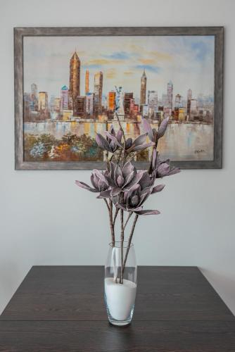 a vase with purple flowers sitting on a table with a painting at Apartmány pri vstupe do Aquaparku in Senec