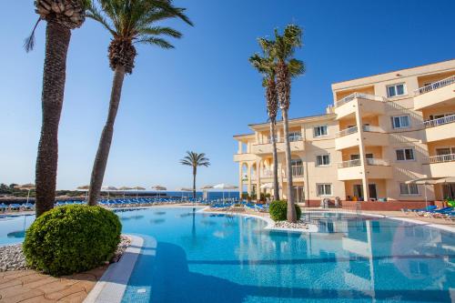 a swimming pool with palm trees in front of a building at Grupotel Tamariscos in Cala'n Bosch