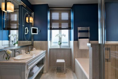 ein Badezimmer mit zwei Waschbecken, einer Badewanne und einem Spiegel in der Unterkunft Hôtel Barrière Le Grand Hôtel Dinard in Dinard