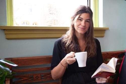 a woman holding a book and a cup of coffee at Ocean Island Inn | Backpackers | Suites in Victoria