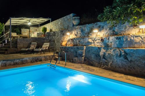 a swimming pool at night with a stone wall at Stone Built Villa Galatia, Poolside & Perfect View in Karés