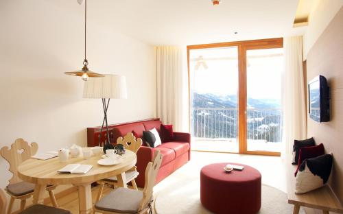 ein Wohnzimmer mit einem Tisch und einem roten Sofa in der Unterkunft Falkensteiner Residences edelweiss in Katschberghöhe