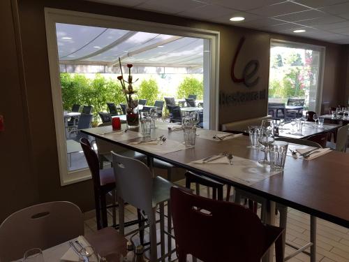 ブラニャックにあるカンパニール トゥールーズ - ブラニャック アエロポルトのテーブルと椅子、大きな窓のあるレストラン