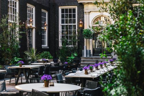 an outdoor restaurant with tables and chairs and purple flowers at The Dylan Amsterdam - The Leading Hotels of the World in Amsterdam