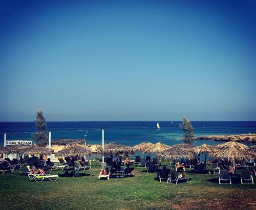 - un groupe de personnes assises dans des chaises sous des parasols de paille sur la plage dans l'établissement Phaedrus Living: Seaside Luxury Villa Anafi, à Paralímni