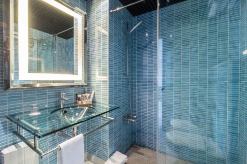 Baño de azulejos azules con lavabo y espejo en Mercure Algeciras en Algeciras