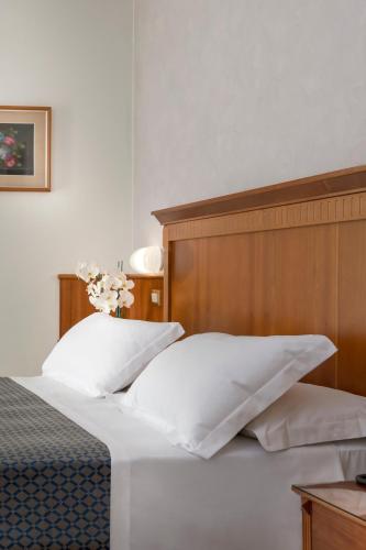 a bed with a wooden head board and white pillows at Hotel Bellevue in Rimini