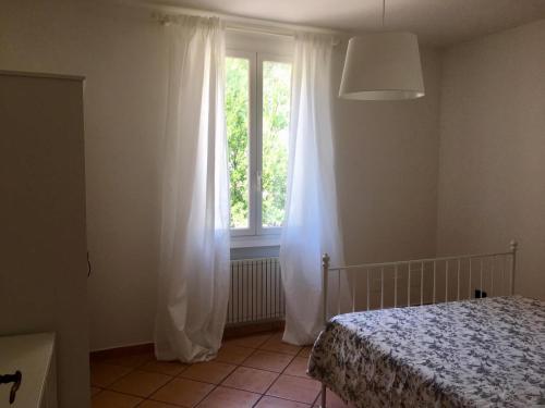 een slaapkamer met een bed en een raam met witte gordijnen bij La casa del Podere in Castellaro