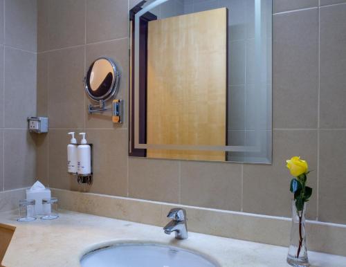 a bathroom sink with a mirror and a vase of flowers at Kingsgate Hotel Doha by Millennium Hotels in Doha