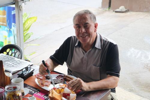 an older man sitting at a table with a plate of food at Hideaway Guest House And Bar in Pattaya Central