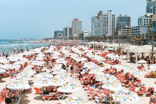 a crowd of people sitting on a beach with umbrellas at Wom Allenby Pod Hotel in Tel Aviv