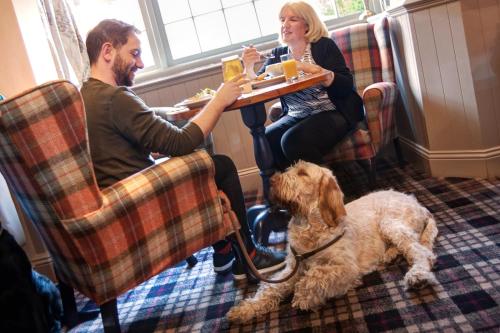 a man and a woman sitting at a table with a dog at The Coniston Inn - The Inn Collection Group in Coniston