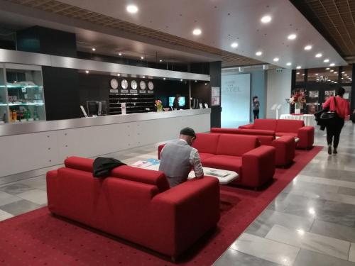 a man sitting on a red couch in a lobby at Hotel SATEL in Poprad