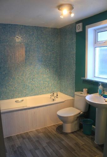 a bathroom with a tub and a toilet and a sink at Arivonie Lochside Cottage in Glencoe