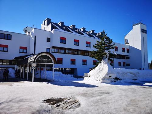 un bâtiment recouvert de neige avec un arbre devant lui dans l'établissement Waldwipfel-Appartement, à Sankt Englmar