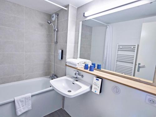 La salle de bains est pourvue d'un lavabo, d'une baignoire et d'un miroir. dans l'établissement Kyriad Lille Est - Hem, à Hem