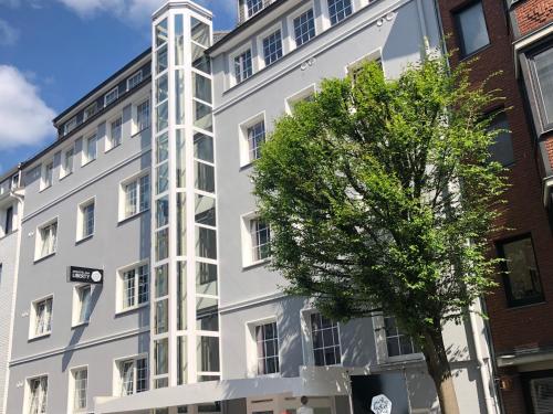 a white building with a tree in front of it at Arthotel ANA Liberty Bremen City in Bremen