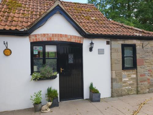 a white house with a black door and a cat sitting outside at The Miners Cottage in Whitecroft