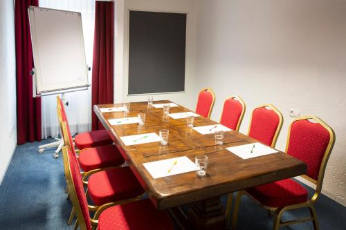 une salle de conférence avec une longue table en bois et des chaises rouges dans l'établissement Elan Hotel, à Limburg an der Lahn