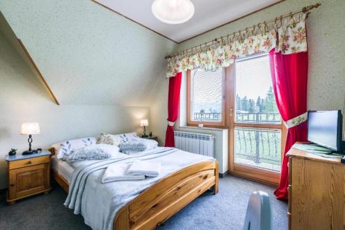 Schlafzimmer mit einem Bett und einem Fenster mit roten Vorhängen in der Unterkunft Willa Cetynka in Zakopane
