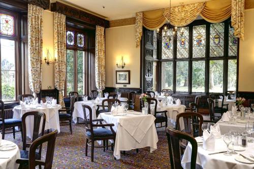 a restaurant with white tables and chairs and windows at Orton Hall Hotel & Spa in Peterborough