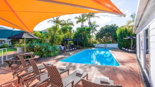 a swimming pool with chairs and an orange umbrella at Scenic Hotel Bay of Islands in Paihia
