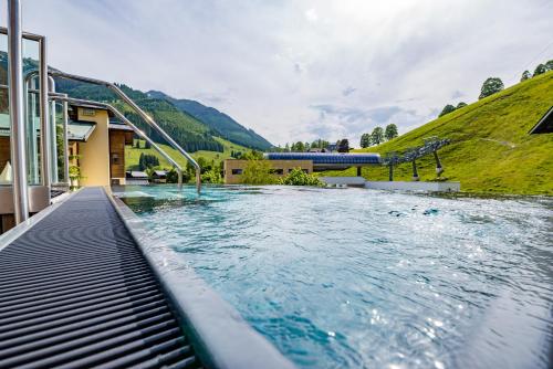 a large swimming pool with a hill in the background at Hotel Kendler in Saalbach Hinterglemm