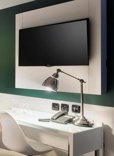 a desk with a lamp and a television on a wall at Days Inn Dessau in Dessau
