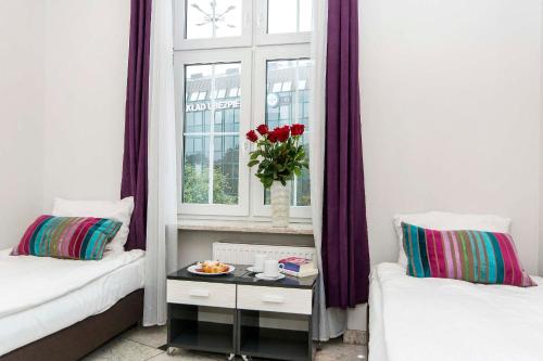 a room with two beds and a window with a vase of flowers at 3 City Hostel in Gdańsk