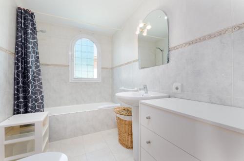 a white bathroom with a sink and a tub and a mirror at Es Repos in Playa de Muro