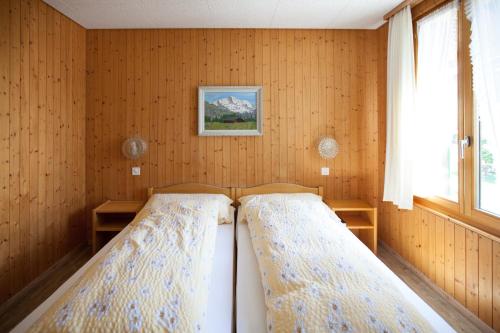 two beds in a room with wooden walls at Hotel Edelweiss in Wengen