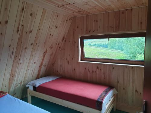 a room with a red bed in a wooden room with a window at Bacówka PTTK Jaworzec in Wetlina