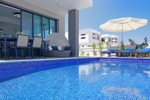 a swimming pool with chairs and an umbrella next to a house at Villa Melody in Protaras