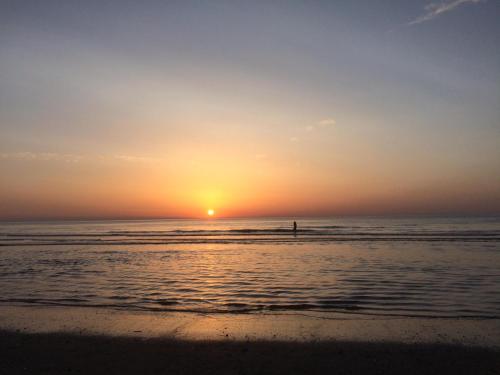 una persona in piedi sulla spiaggia che guarda il tramonto di Cottage Fleuri a Koksijde