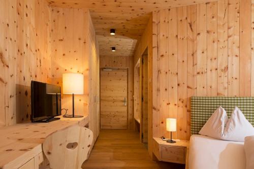 - une chambre avec des murs en bois, un lit et une télévision dans l'établissement Hotel Schoenblick, à Sesto