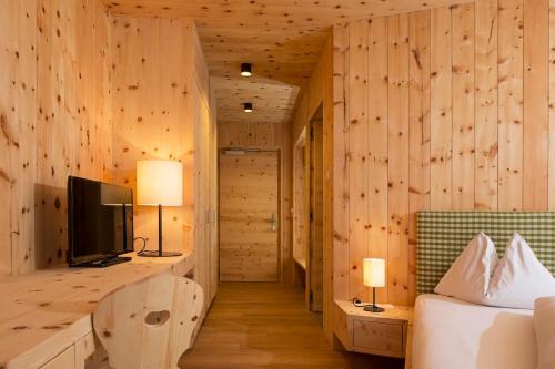 a bedroom with wooden walls and a bed and a television at Hotel Schoenblick in Sesto