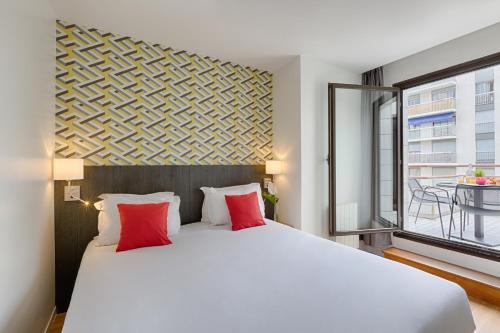 a bedroom with a large white bed with red pillows at Citadines Austerlitz Paris in Paris