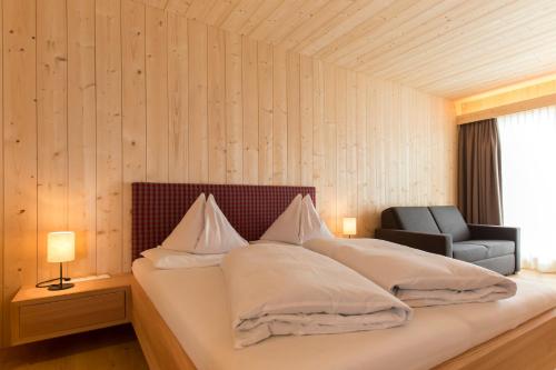 Cette chambre comprend un lit avec des oreillers blancs et une chaise. dans l'établissement Hotel Schoenblick, à Sesto