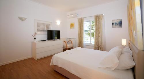 ein weißes Schlafzimmer mit einem Bett und einem TV in der Unterkunft Vila Luz in Vilamoura