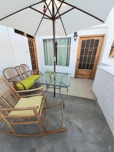 a patio with chairs and a glass table and an umbrella at El Huerto Hostel in Ica