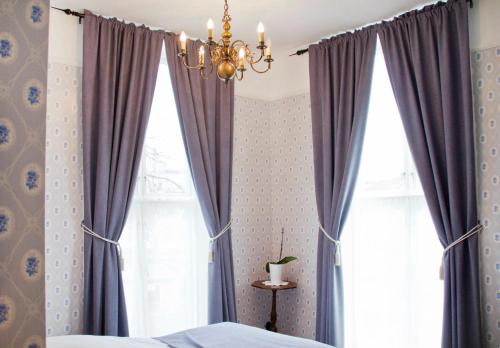 a bedroom with purple curtains and a chandelier at Hotel Kong Carl - Unike Hoteller in Sandefjord