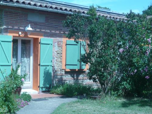a brick house with green shutters and a tree at Le Soubiran in Bérat