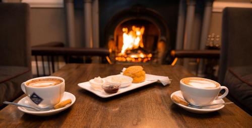 two cups of coffee on a wooden table with a fireplace at Brandon House Hotel in New Ross