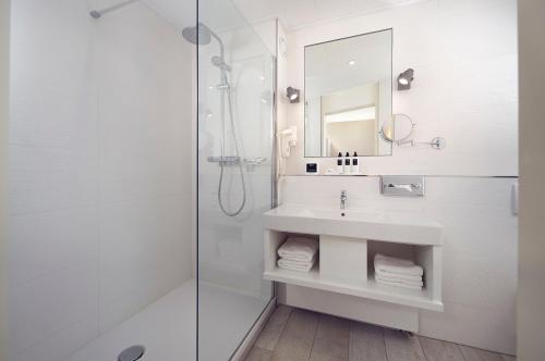 ein weißes Bad mit einem Waschbecken und einer Dusche in der Unterkunft WestCord Hotel Noordsee in Nes