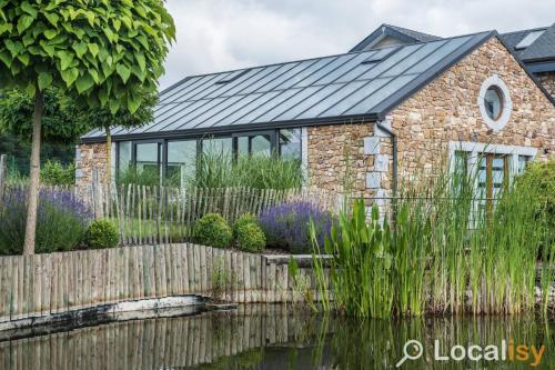 a stone house with a solar roof next to a pond at Thermes Oppidum in Theux