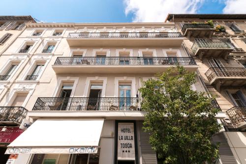 a tall white building with balconies and a tree at Hôtel La Villa Tosca in Cannes