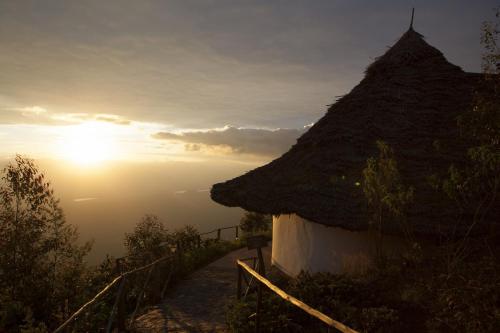 a hut with a grass roof with the sunset in the background at Mambo View Point in Ndungu