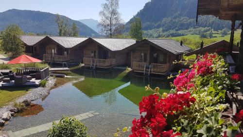 a group of wooden cabins with a river and flowers at Golf- und Sporthotel Moarhof in Walchsee
